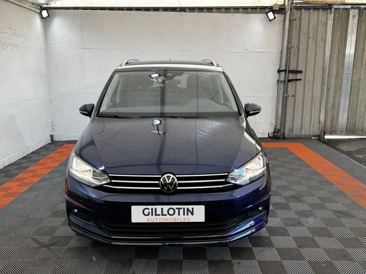 Vue avant d'un Volkswagen Touran bleu 2024 avec calandre chromée et phares LED dans un garage.