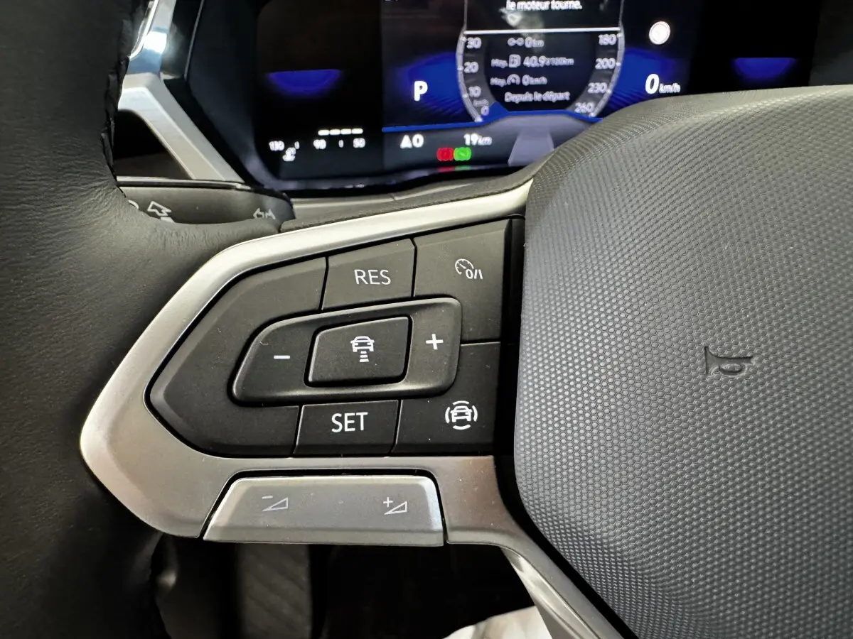 Gros plan sur les commandes de régulateur de vitesse au volant cuir du Volkswagen Touran 2024, affichage numérique en arrière-plan.