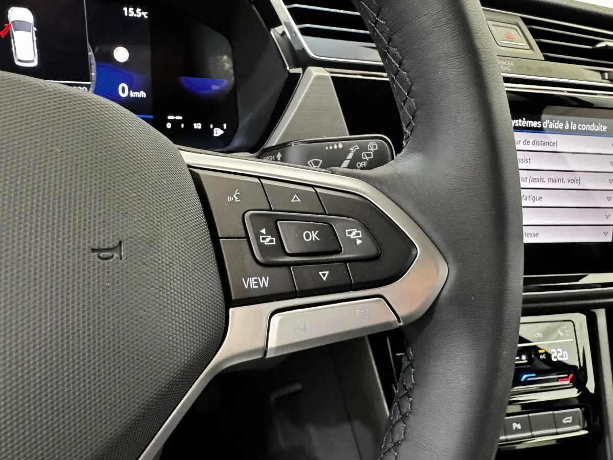 Gros plan sur le volant cuir noir du Volkswagen Touran 2024 avec commandes multifonctions et tableau de bord digital.