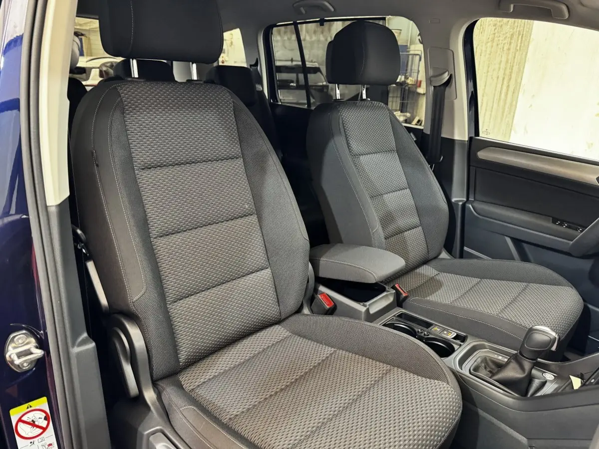Vue intérieure côté avant droit du Volkswagen Touran bleu 2024, montrant les sièges tissu gris et la console centrale.