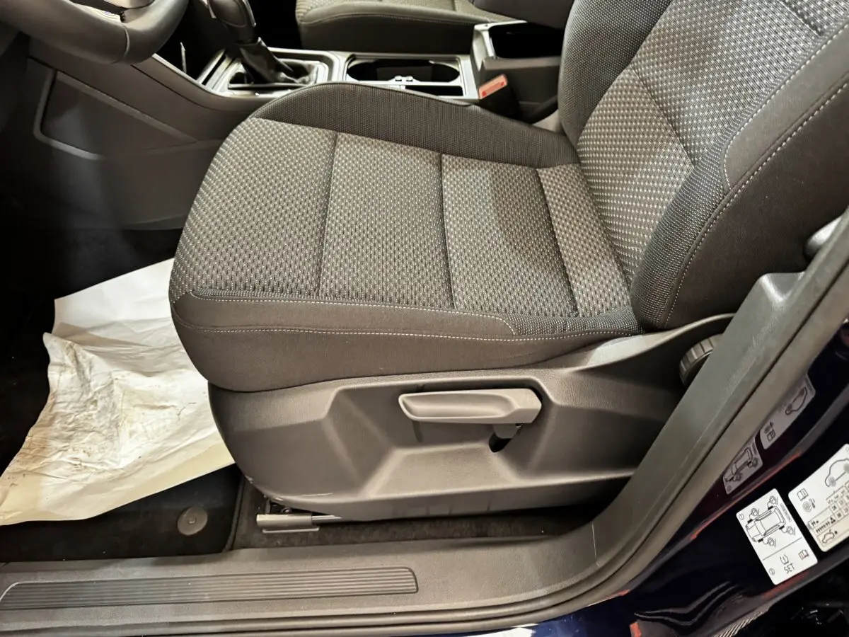 Gros plan sur le siège avant droit tissu gris foncé du Volkswagen Touran 2024, avec réglage manuel et partie de la portière bleue visible.