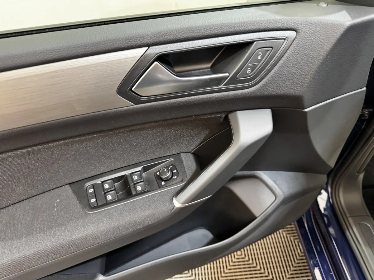 Vue intérieure sur la porte avant gauche bleu foncé d'un Volkswagen Touran 2024 avec commandes de vitres et verrouillage.
