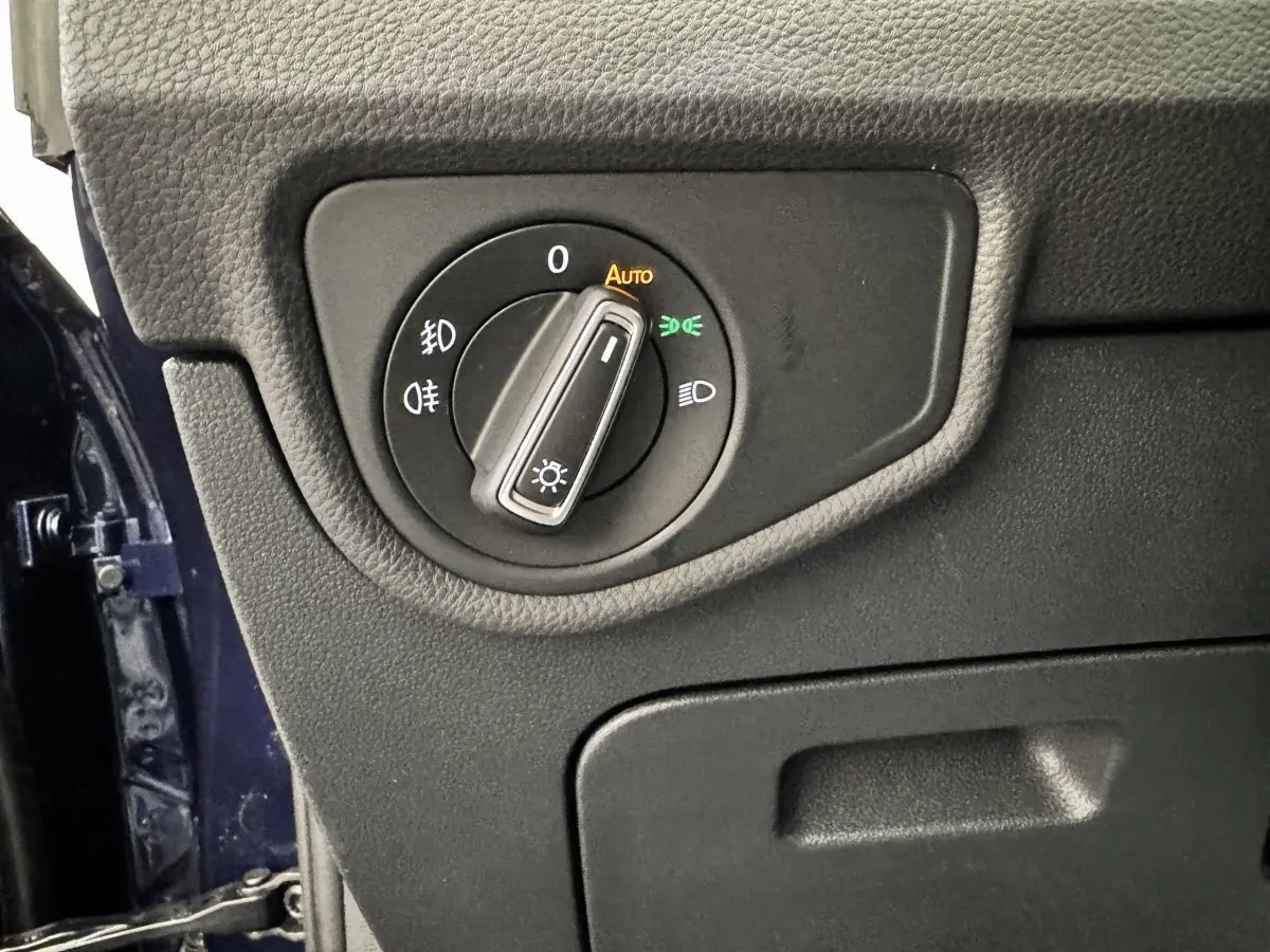 Gros plan sur le bouton de commande des phares à gauche du tableau de bord d’un Volkswagen Touran bleu 2024.