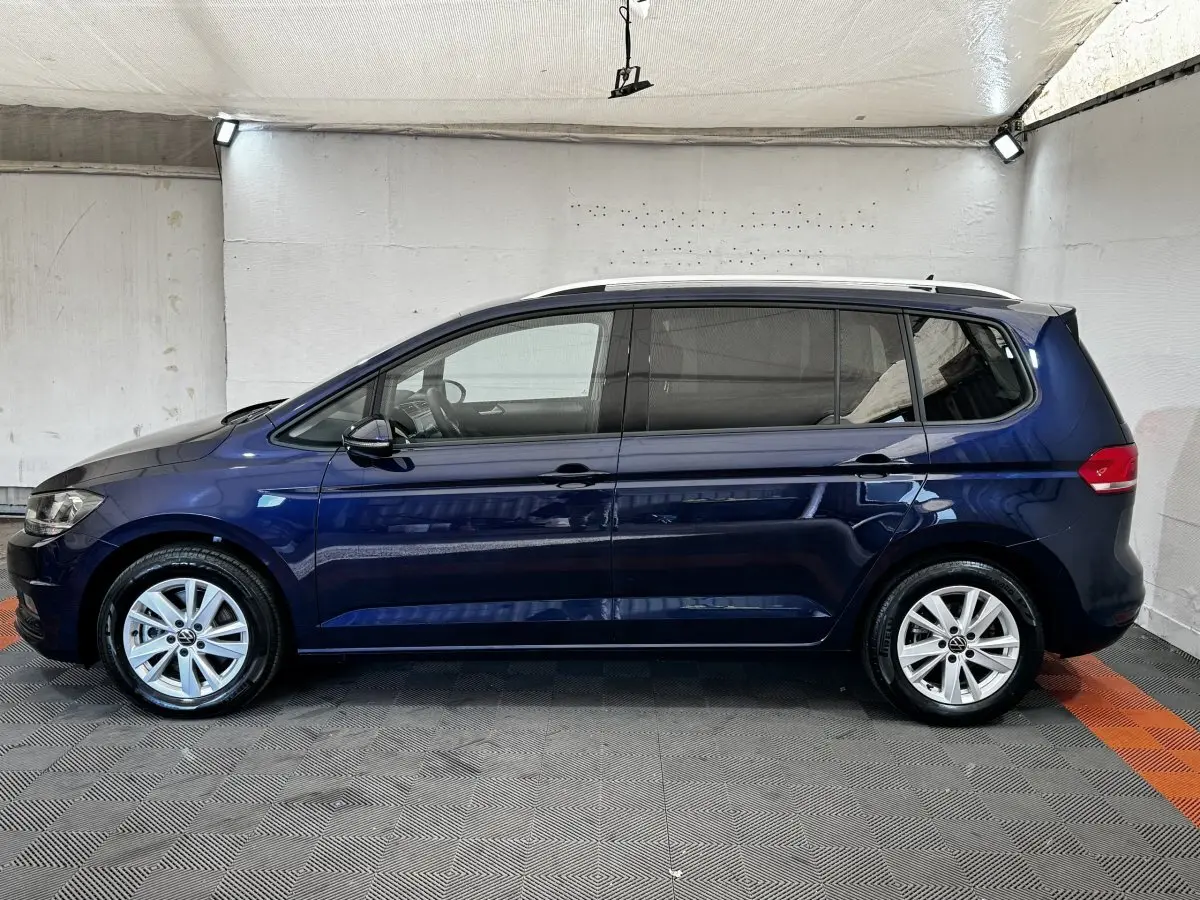 Volkswagen Touran bleu 2024 vue de profil côté gauche dans un espace intérieur éclairé.