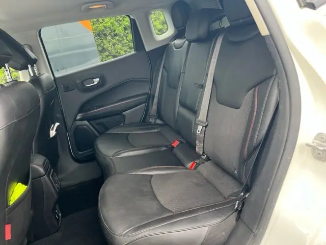 Vue intérieure arrière droite du Jeep Compass 2020 blanc, sièges noirs en cuir avec surpiqûres rouges et ceintures de sécurité visibles.
