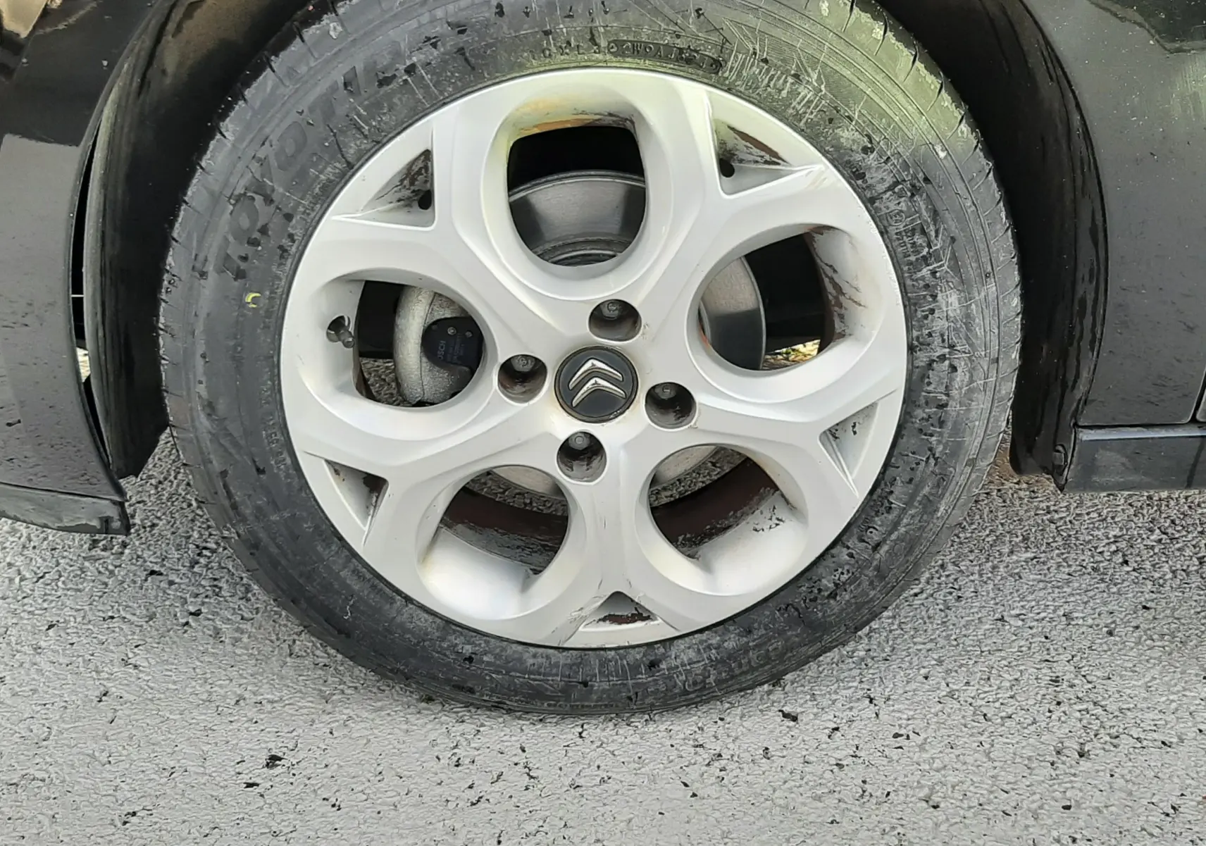 Gros plan sur la roue avant gauche d'une Citroën C3 noire de 2016 avec jante alliage et pneu usé.