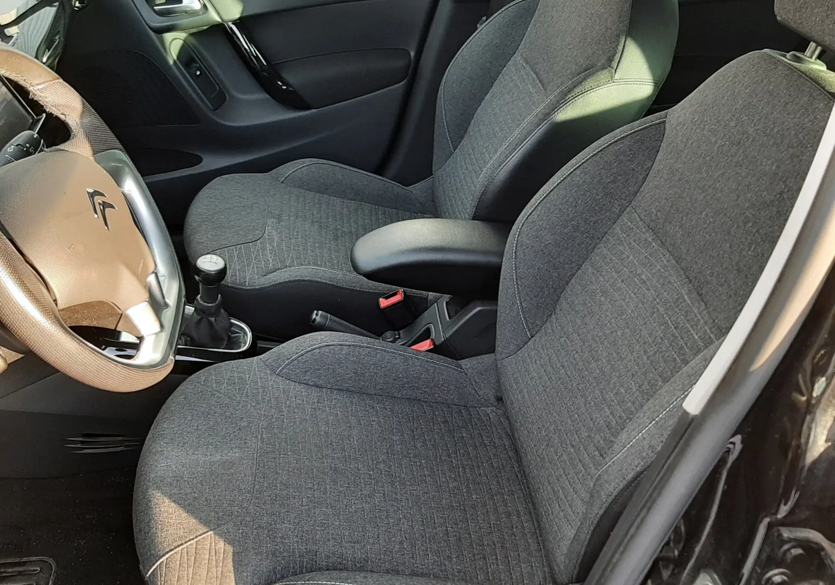 Intérieur de la Citroën C3 noire, vue côté gauche montrant les sièges en tissu gris et le volant avec levier de vitesse manuel.