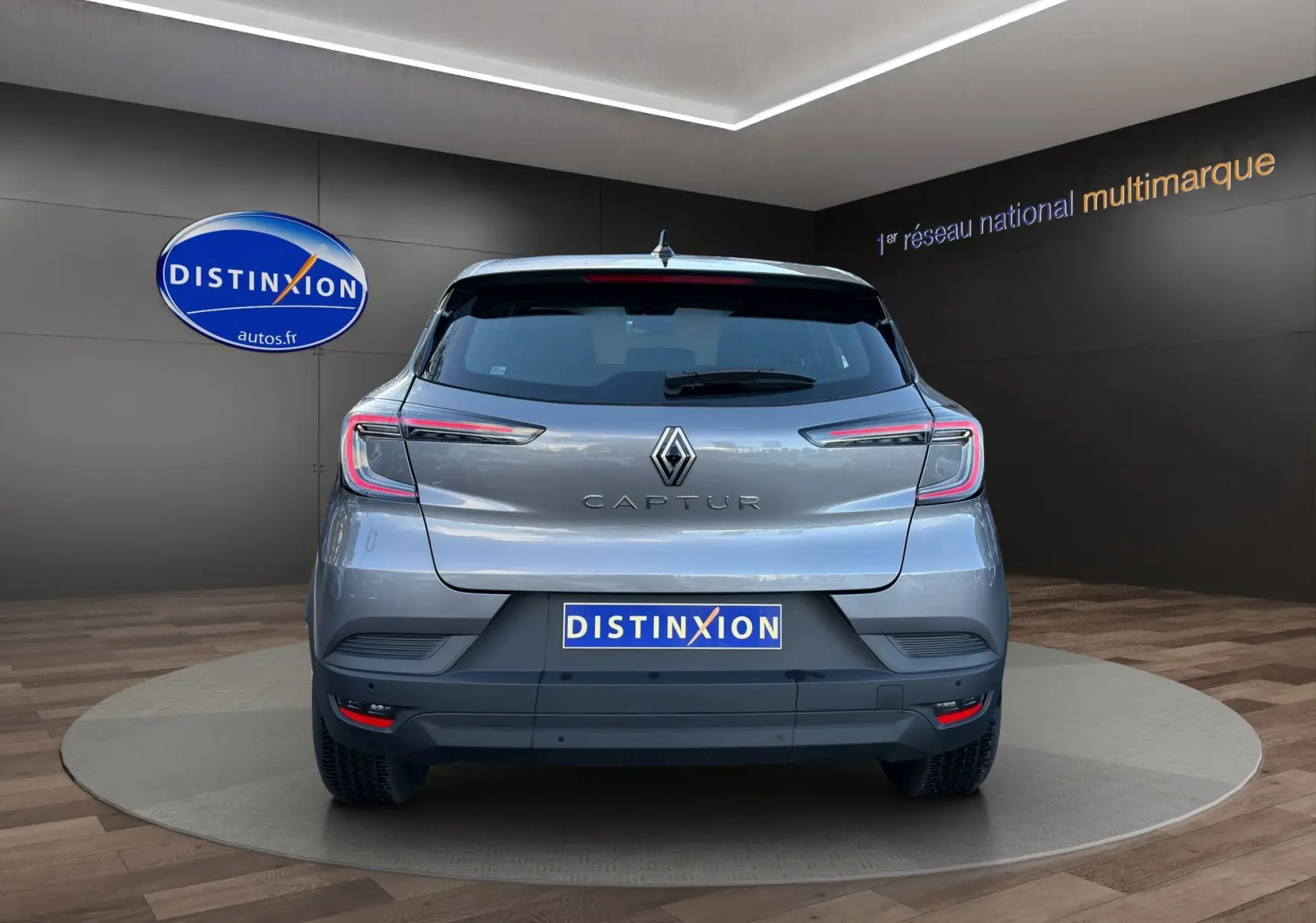 Vue arrière du Renault Captur 2024 gris Cassiopée avec toit noir, feux LED et logo distinctif sur fond showroom.