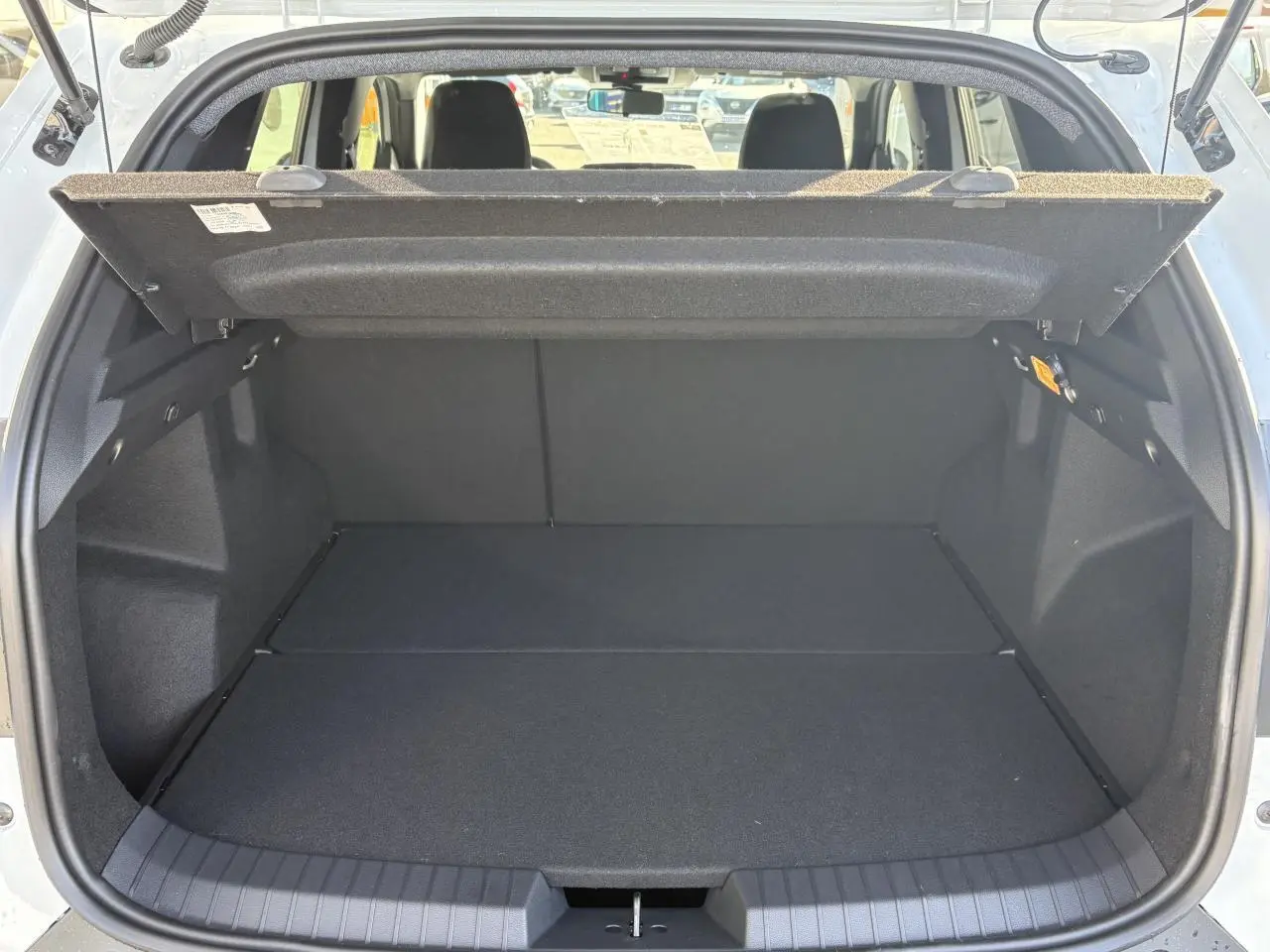 Coffre ouvert vu de l'arrière d'un Dacia Duster blanc métallisé avec cache-bagages relevé et banquette arrière visible.