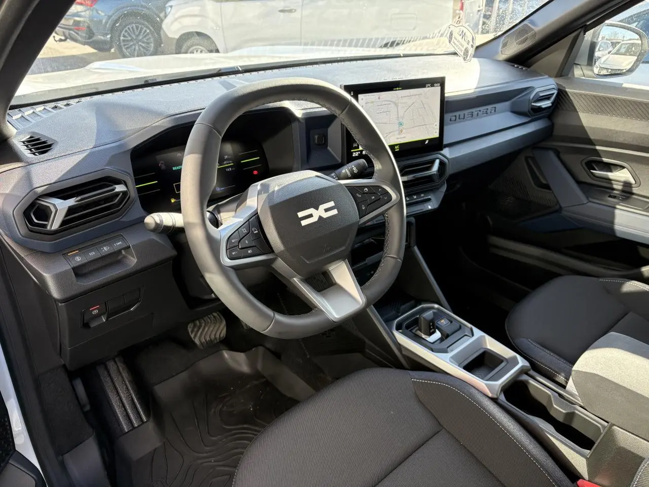 Vue intérieure côté conducteur du Dacia Duster 2024 hybride, avec volant multifonction et écran tactile central.