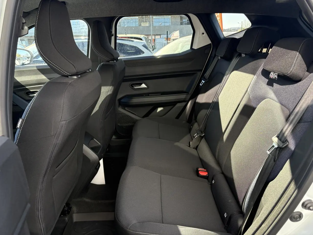 Vue intérieure côté droit de la banquette arrière noire du Dacia Duster 2024 avec appuie-têtes et ceintures de sécurité visibles.