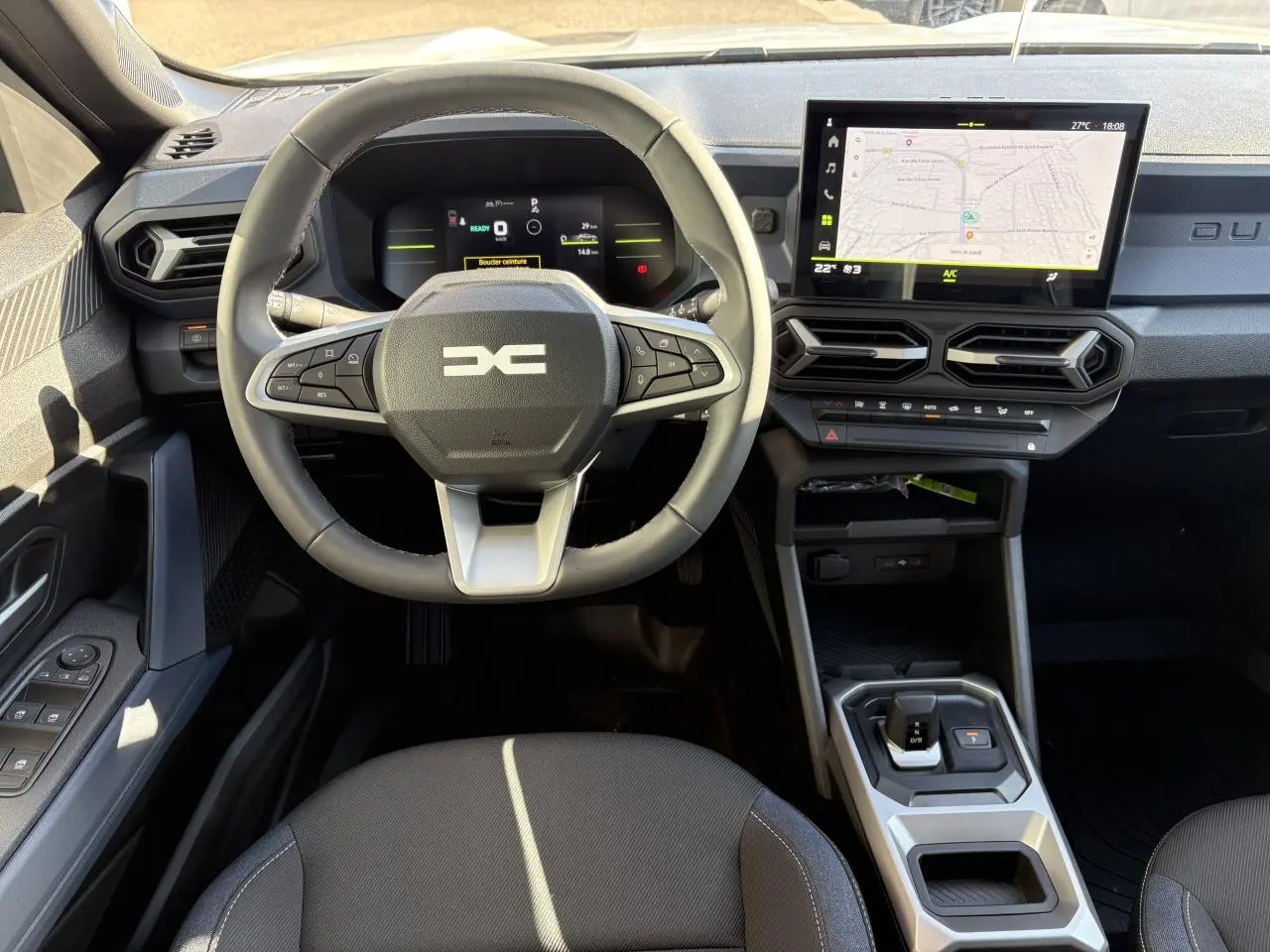 Vue intérieure frontale du tableau de bord du Dacia Duster 2024, avec volant multifonction, écran tactile et sellerie Denim noire.