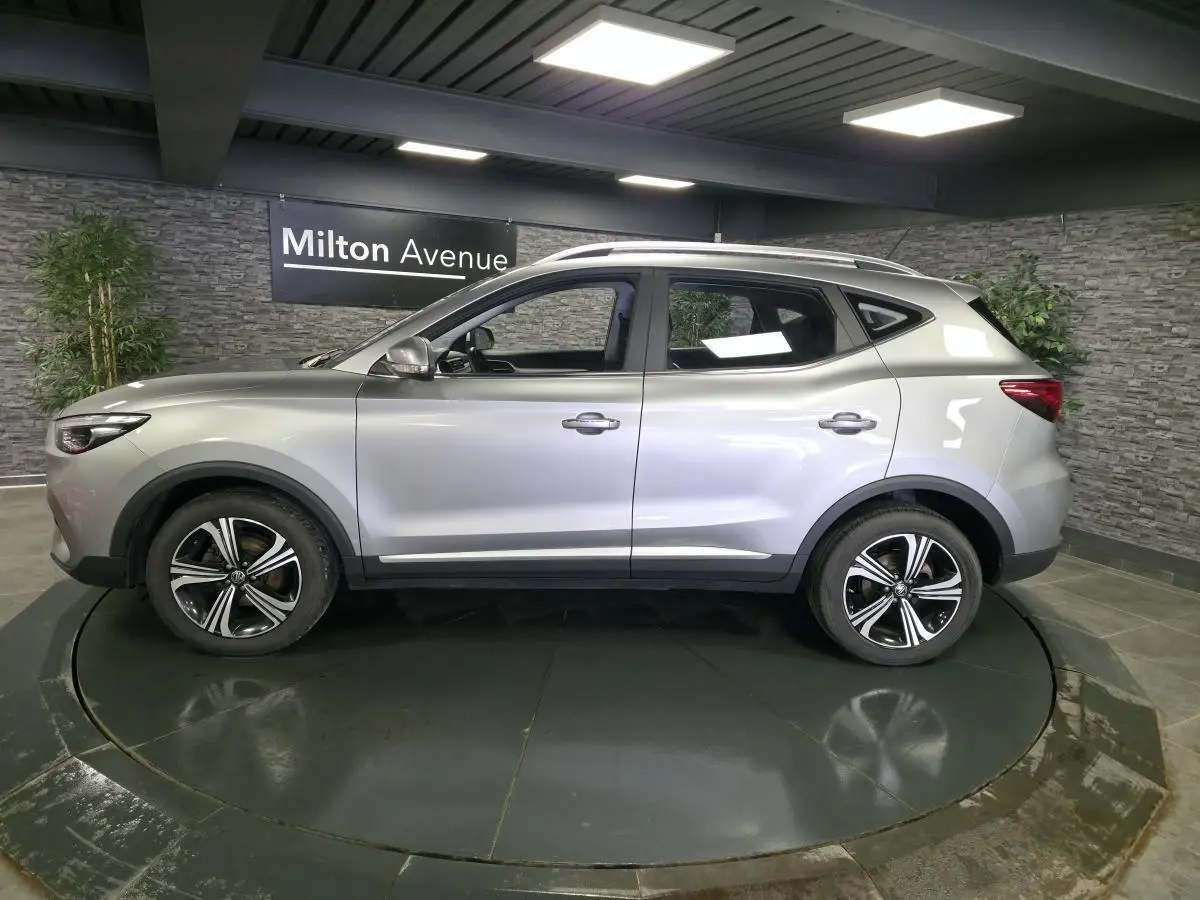Vue de profil côté gauche du SUV MG ZS gris métallisé avec jantes alliage 17 pouces dans un showroom.