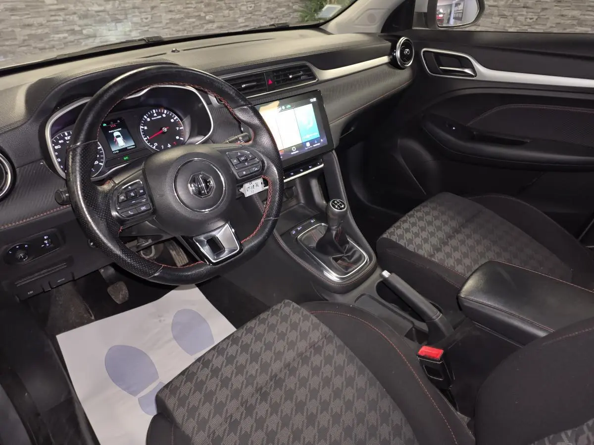 Intérieur de MG ZS 2023 vu côté conducteur, volant cuir, console centrale avec écran tactile et levier de vitesses manuel.