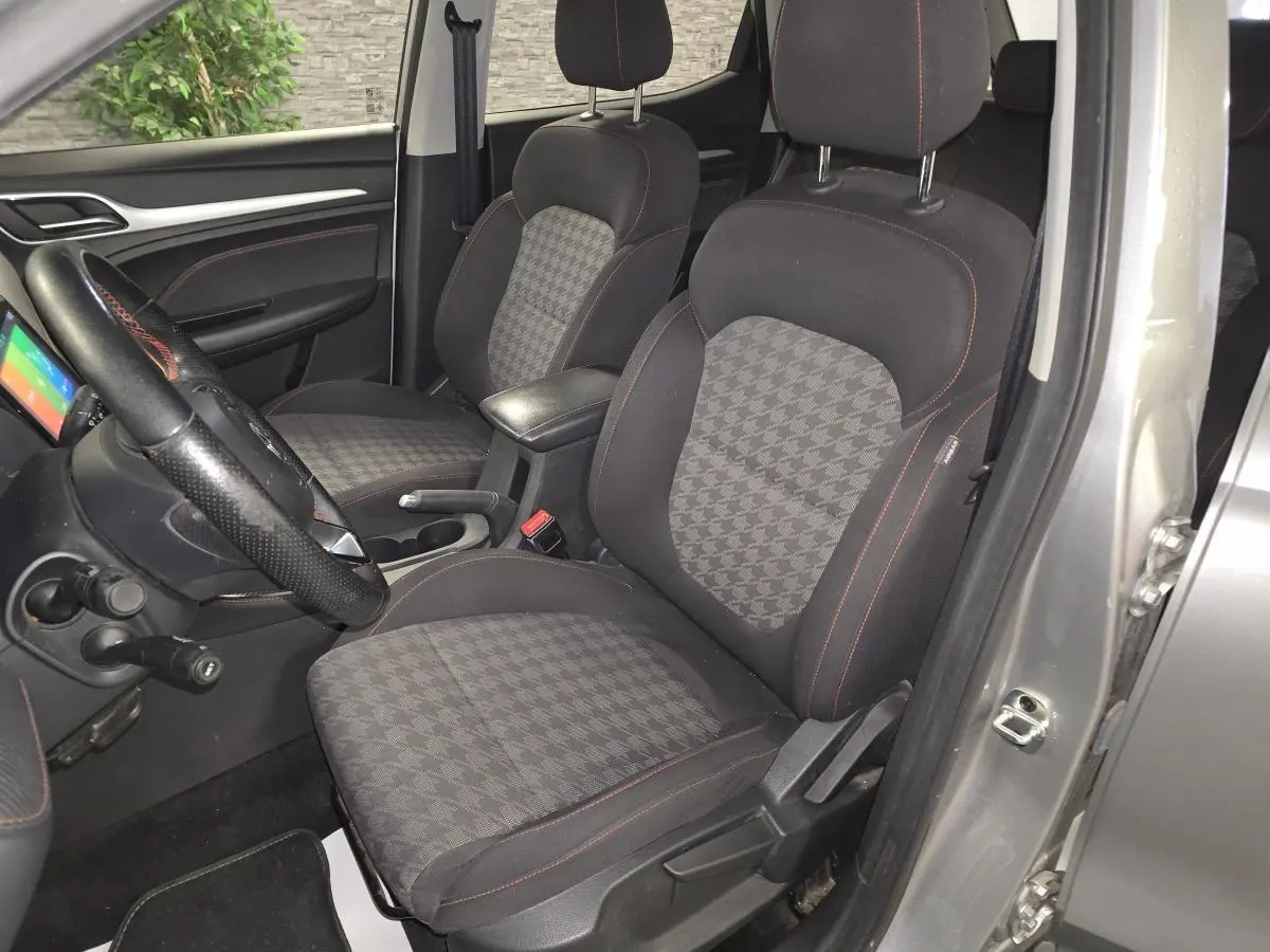 Vue intérieure côté conducteur du MG ZS gris 2023, sièges tissu à motif pied-de-poule et volant cuir avec surpiqûres rouges.