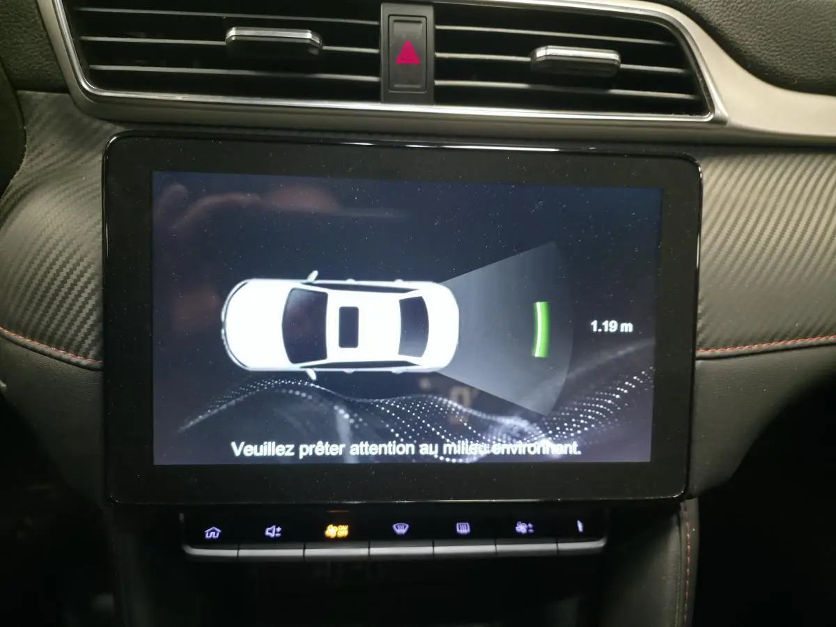 Écran tactile intérieur montrant l'alerte de distance de stationnement du MG ZS gris, avec tableau de bord en carbone.