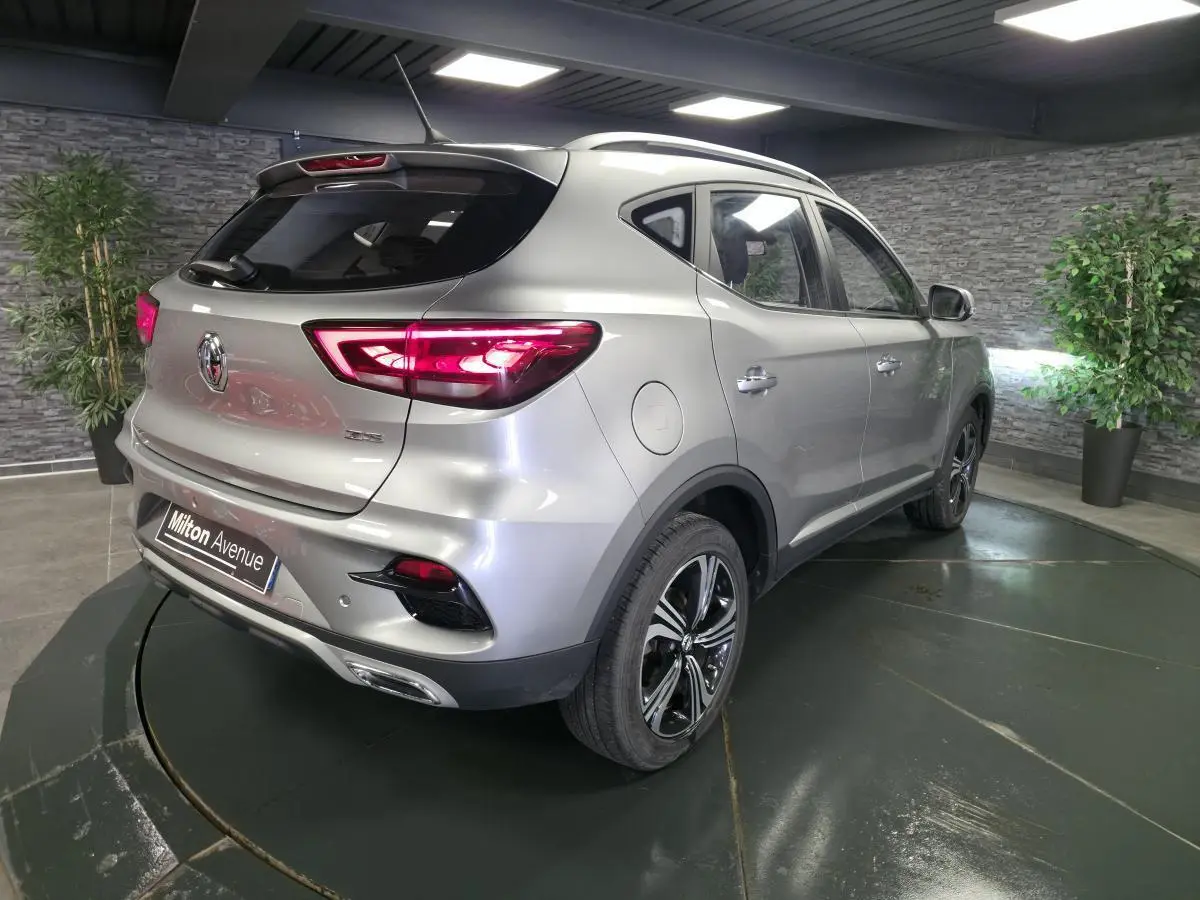 Vue 3/4 arrière droite du SUV MG ZS gris métallisé avec feux arrière LED allumés et jantes alliage noires.