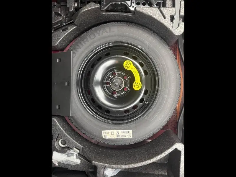 Roue de secours noire avec étiquette jaune dans le coffre d'une FIAT 500X 2024 Rouge Passione pastel.