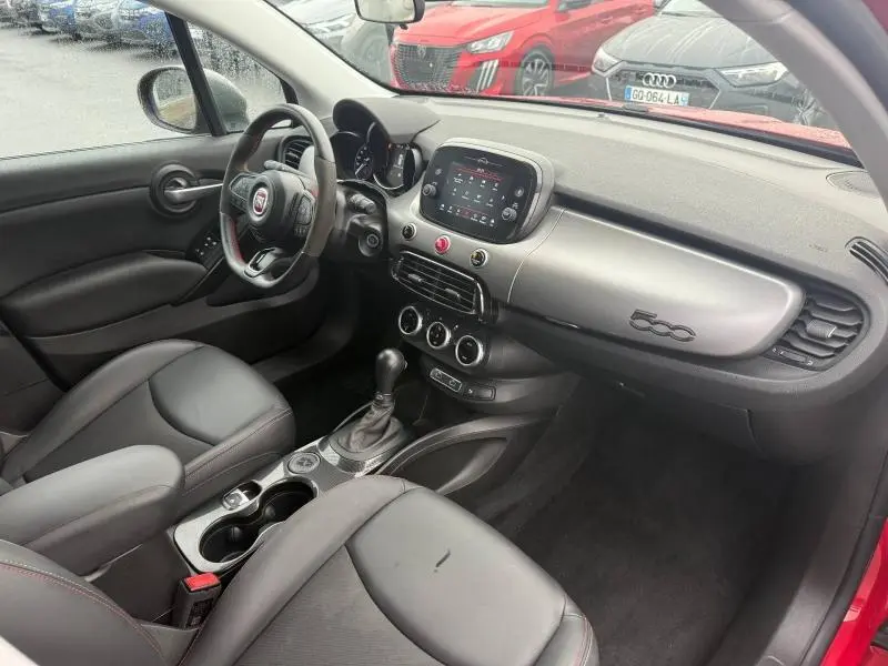 Vue intérieure côté conducteur de la Fiat 500X 2024 rouge Passione pastel, avec tableau de bord et console centrale modernes.