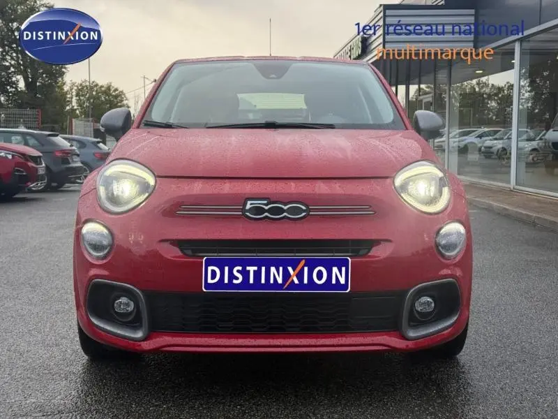 Vue frontale d'une FIAT 500X rouge Passione pastel avec phares allumés sur un sol humide.