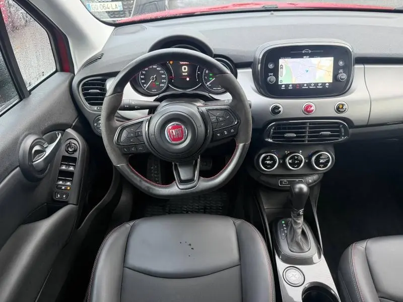 Vue intérieure centrée sur le poste de conduite du Fiat 500X 2024 rouge, avec volant multifonction et écran tactile de navigation.