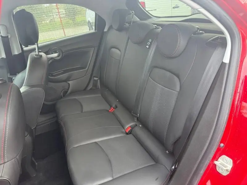 Vue intérieure arrière droite du FIAT 500X 2024 rouge Passione pastel, sièges en cuir noir avec surpiqûres rouges.