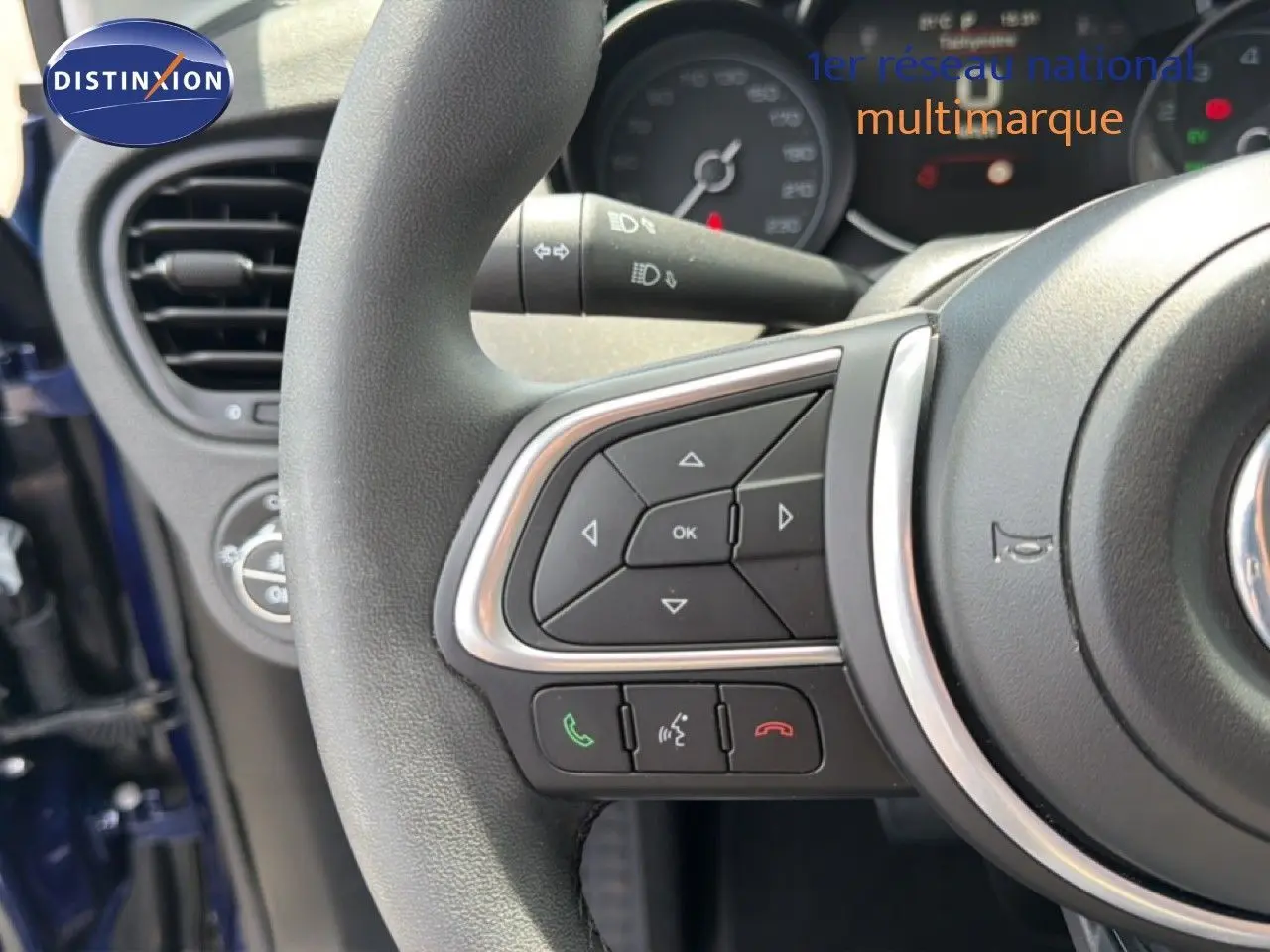 Gros plan sur le volant avec commandes intégrées du Fiat 500X bleu Venezia, tableau de bord partiellement visible en arrière-plan.