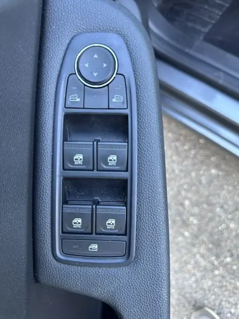 Gros plan sur les commandes des vitres électriques et des rétroviseurs côté conducteur d'une Renault Clio gris 2025.