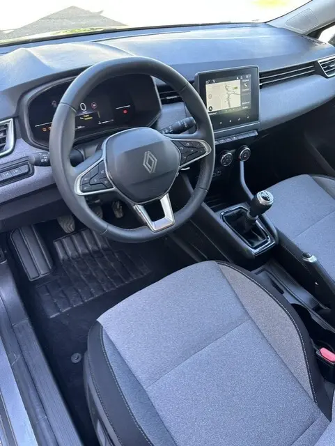Vue intérieure côté conducteur de la Renault Clio gris 2025, avec volant multifonction, écran tactile et boîte manuelle.