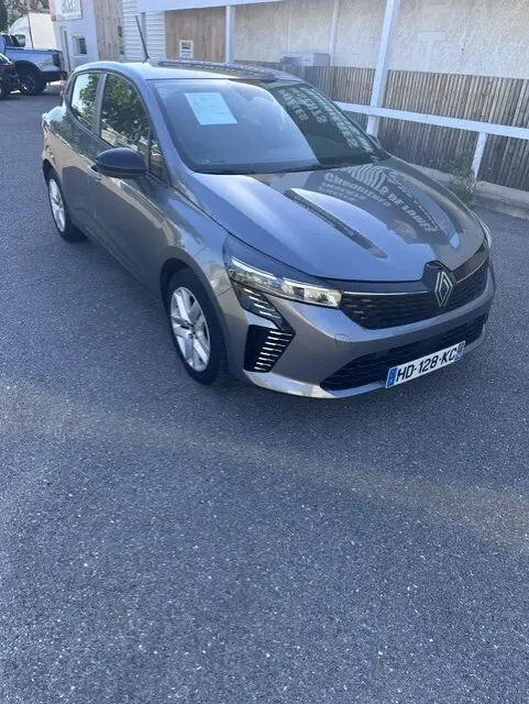 Renault Clio gris 2025 vue 3/4 avant droit, avec calandre moderne et feux LED distinctifs.