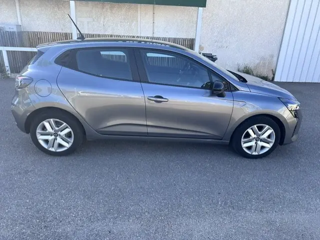 Profil droit d'une Renault Clio gris 2025 avec vitres surteintées et jantes alliage, stationnée sur sol goudronné.