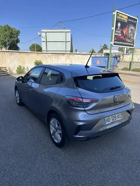 Renault Clio gris 2025 vue 3/4 arrière droit, vitres surteintées et antenne sur le toit dans un parking extérieur.