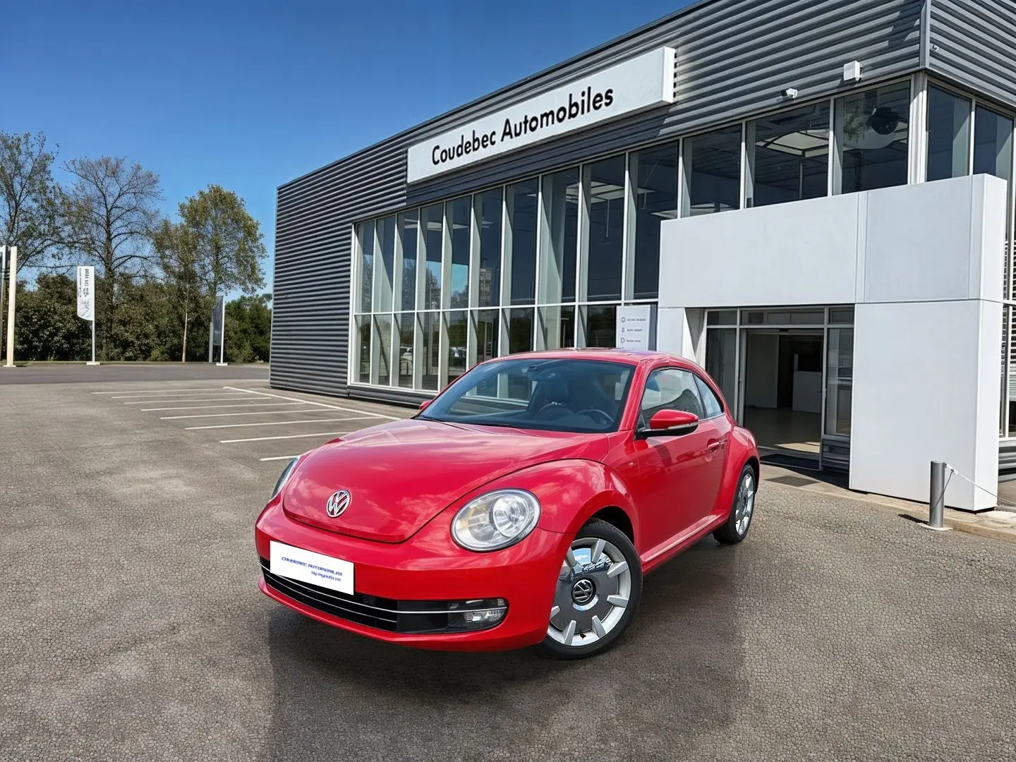 Volkswagen Coccinelle rouge vue en 3/4 avant droit, stationnée devant un bâtiment commercial moderne.