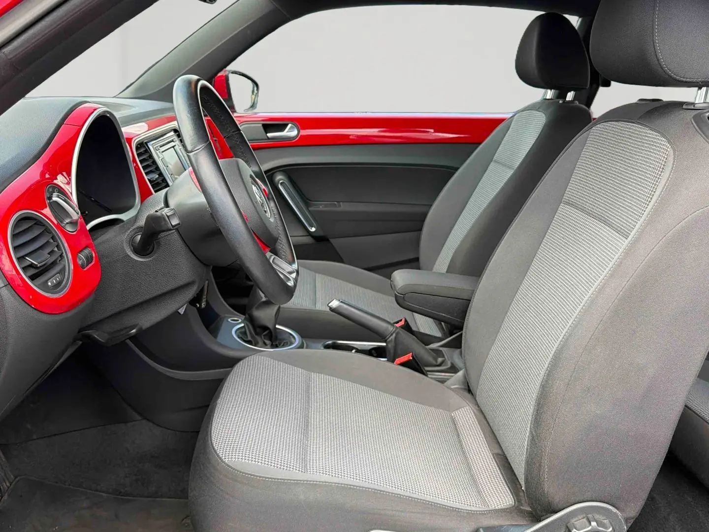 Intérieur côté conducteur de la Volkswagen Coccinelle 2012, tableau de bord rouge Tornade et sièges gris.