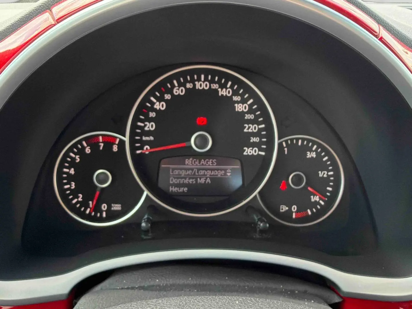Vue rapprochée du tableau de bord de la Volkswagen Coccinelle rouge, affichant les compteurs et l'écran de réglages.