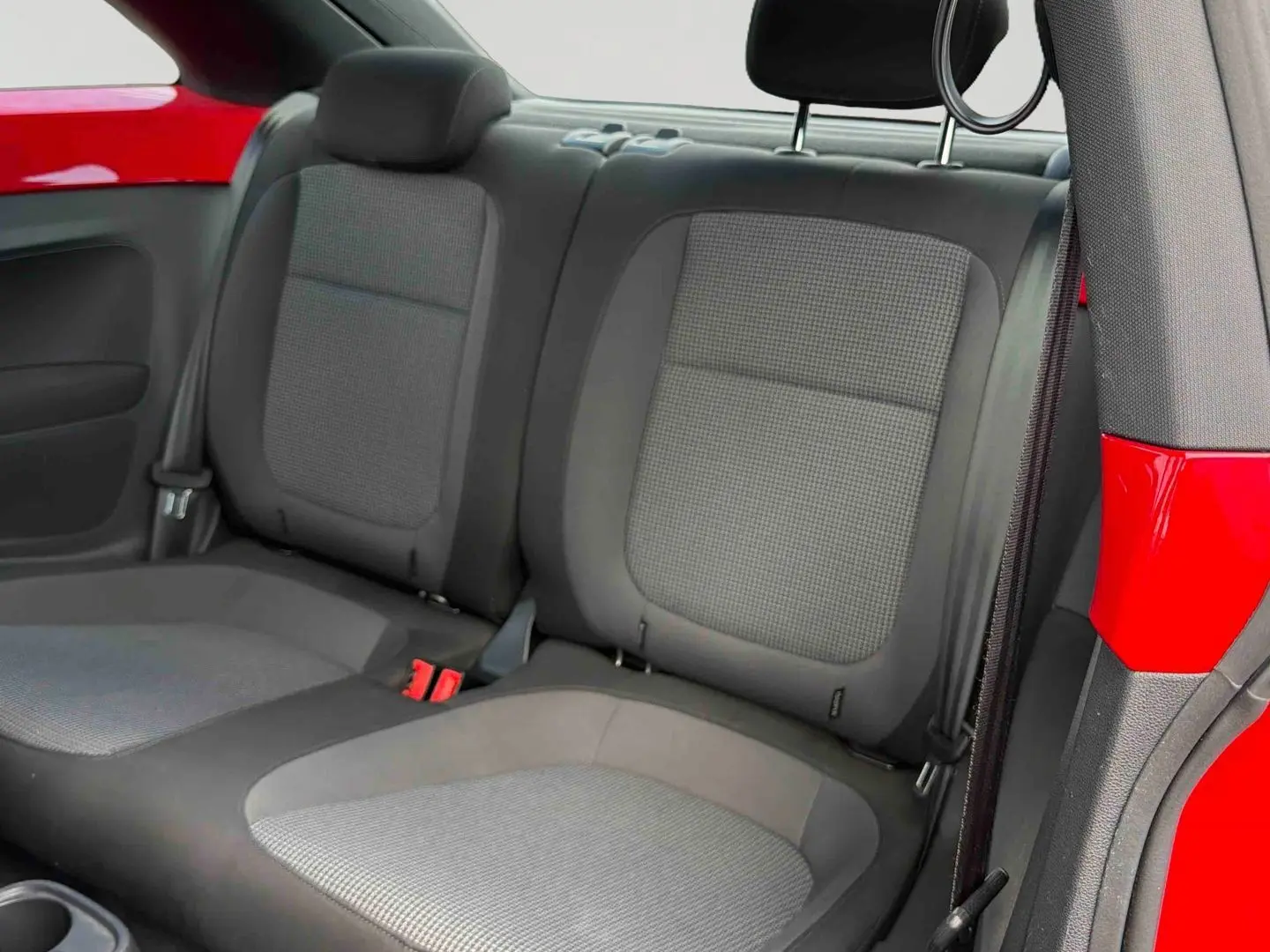 Vue intérieure arrière droite de la Volkswagen Coccinelle rouge, montrant les sièges arrière gris et la carrosserie rouge Tornade.
