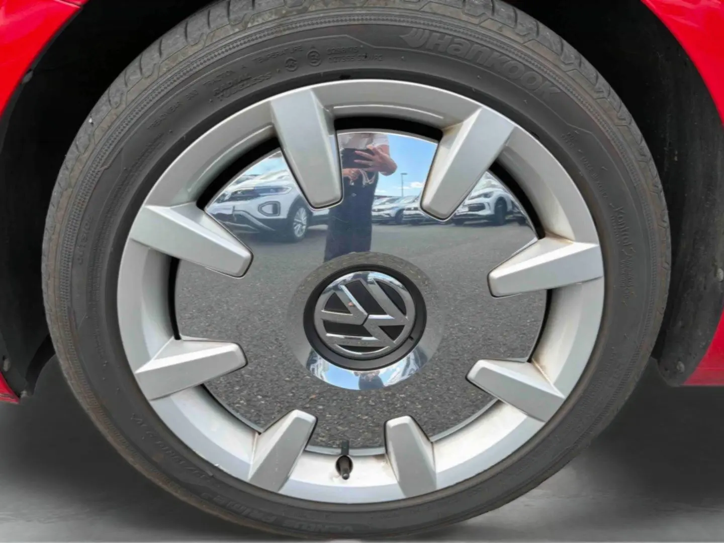 Gros plan sur la jante 18 pouces Disc argentée avec logo Volkswagen, entourée du pneu Hankook sur une Volkswagen Coccinelle rouge.