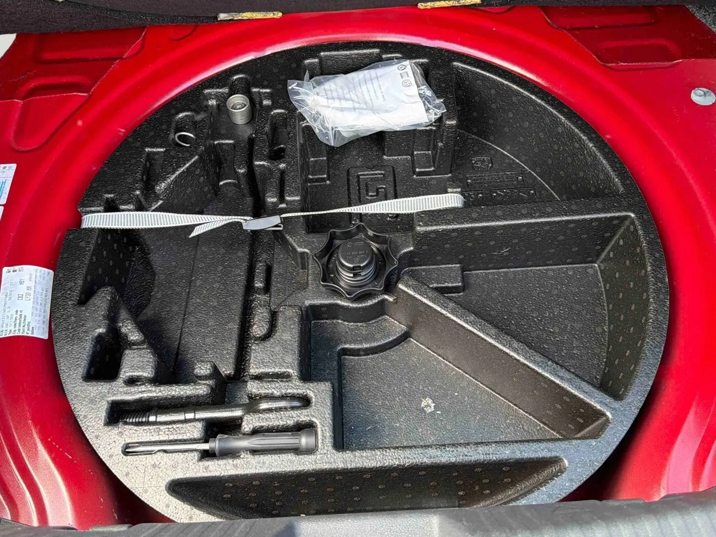 Vue plongeante sur le coffre à outils vide de la Volkswagen Coccinelle rouge, montrant l'emplacement des accessoires.