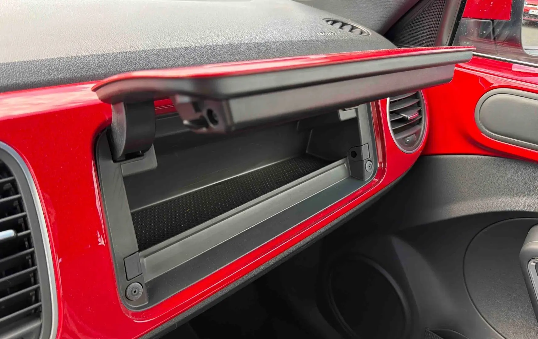 Vue intérieure côté passager de la Volkswagen Coccinelle rouge de 2012, boîte à gants ouverte et garnitures rouges visibles.