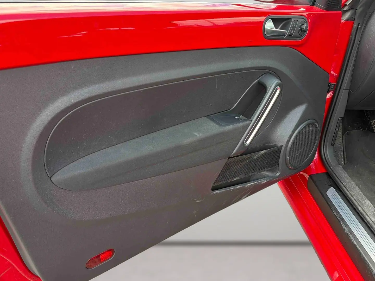 Vue rapprochée de la porte avant gauche rouge de la Volkswagen Coccinelle 2012 avec panneau intérieur noir et poignée argentée.