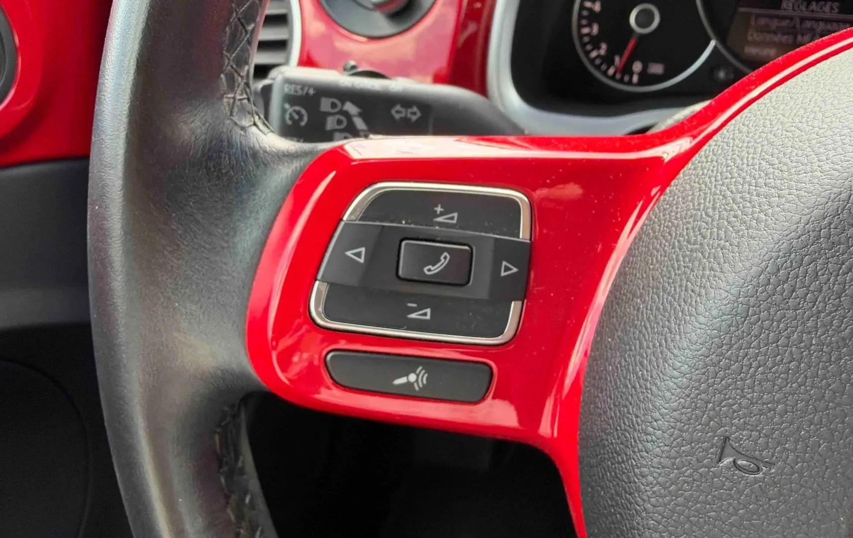 Gros plan sur la partie gauche du volant rouge et noir de la Volkswagen Coccinelle avec commandes multifonctions.