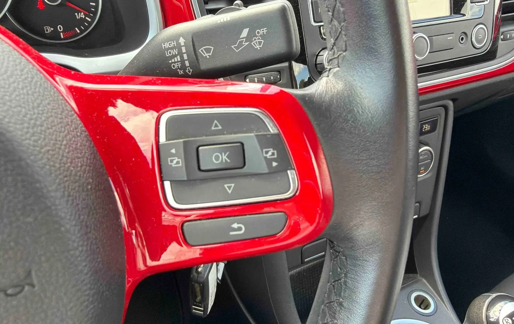 Gros plan sur le volant cuir multifonction rouge et noir de la Volkswagen Coccinelle avec commandes intégrées.