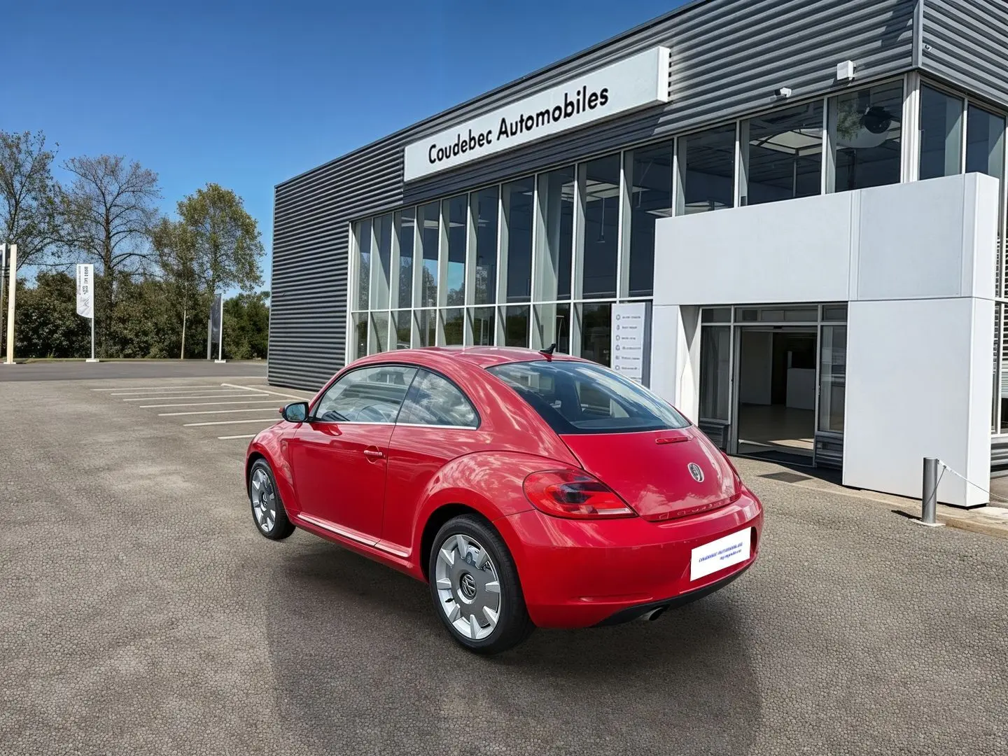 Volkswagen Coccinelle rouge vue en 3/4 arrière droit, avec jantes 18 pouces et feux arrière LED, devant un showroom.