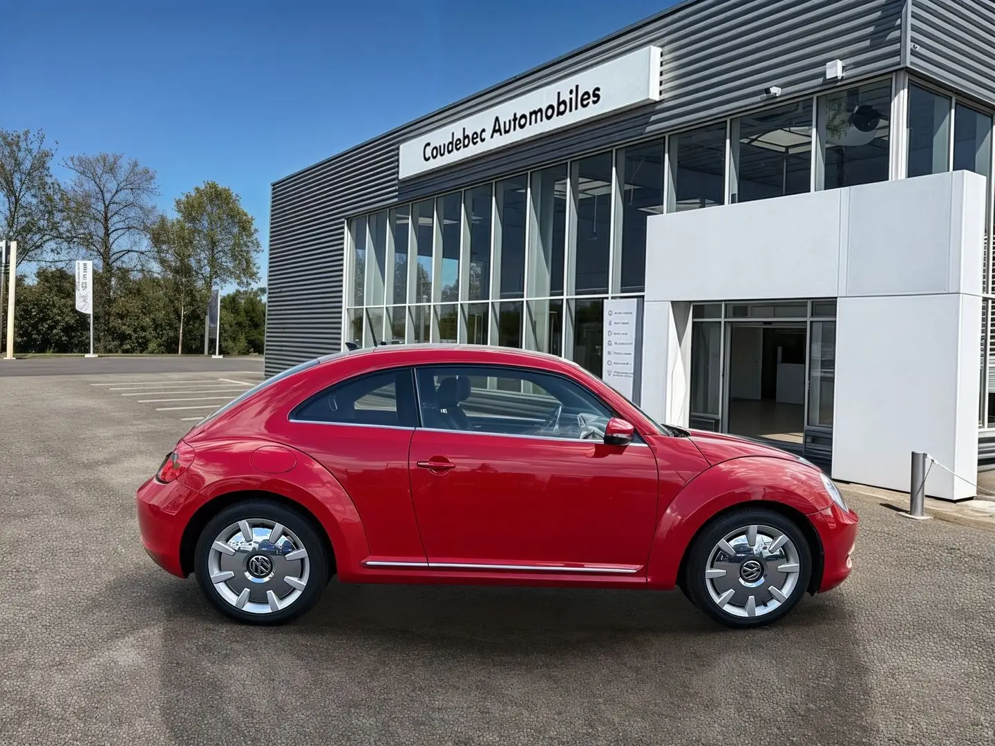 Vue de profil droit d'une Volkswagen Coccinelle rouge Tornade avec jantes 18 pouces Disc, stationnée devant un concessionnaire.