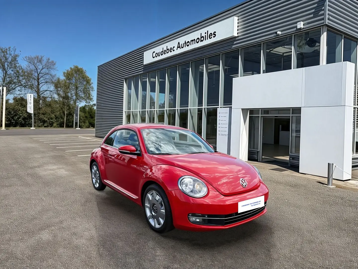 Volkswagen Coccinelle rouge vue 3/4 avant droit, avec jantes 18 pouces, stationnée devant un bâtiment commercial.