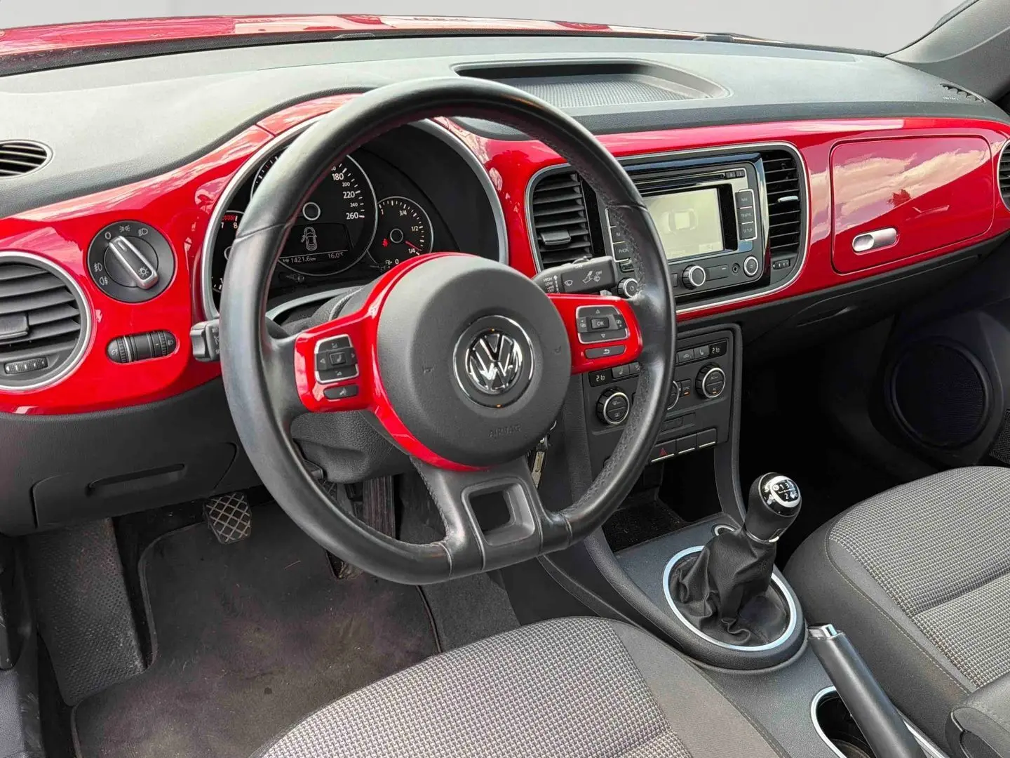 Vue intérieure côté conducteur de la Volkswagen Coccinelle 2012 avec tableau de bord rouge Tornade et volant cuir multifonction.
