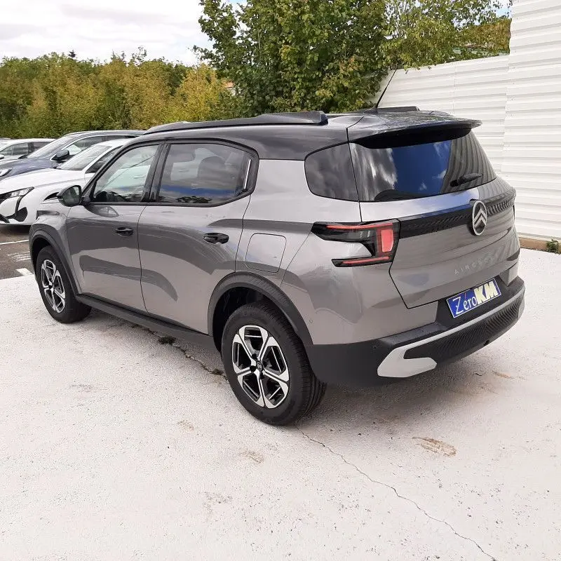 Vue 3/4 arrière gauche d'un Citroën C3 Aircross gris Mercury avec toit noir, jantes modernes et feux arrière LED distinctifs.