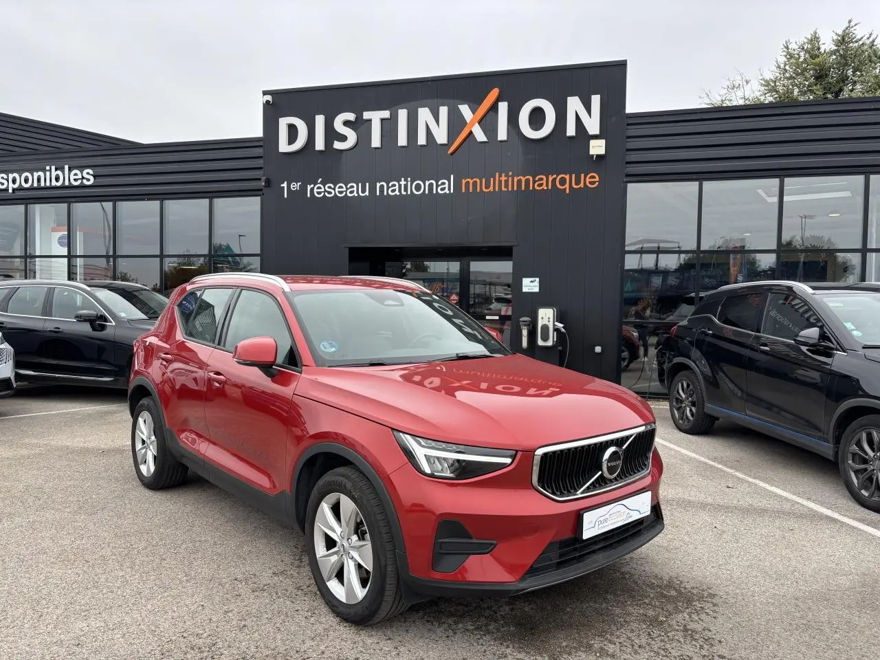 Volvo XC40 Fusion Red en 3/4 avant gauche, avec calandre distinctive et jantes alliage 18 pouces visibles.
