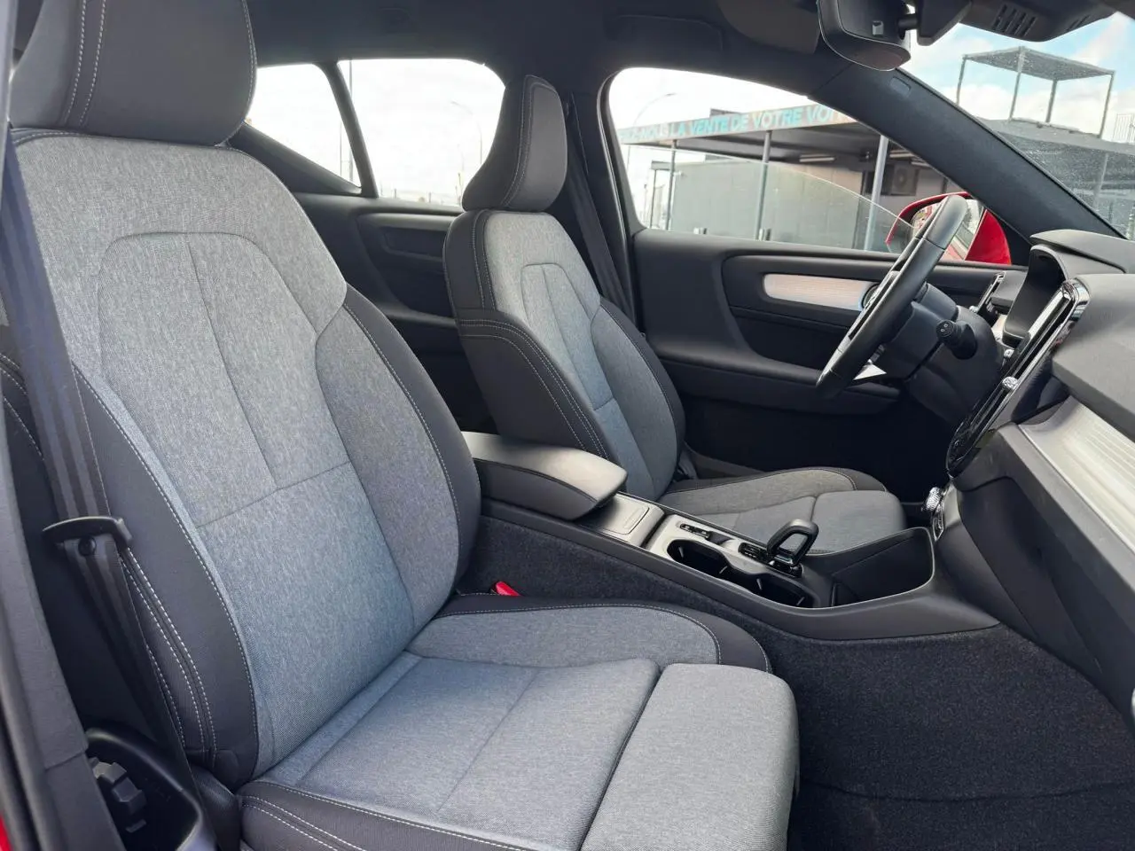 Intérieur du Volvo XC40 B3 2024 vu côté droit, sièges tissu gris clair avec console centrale noire.