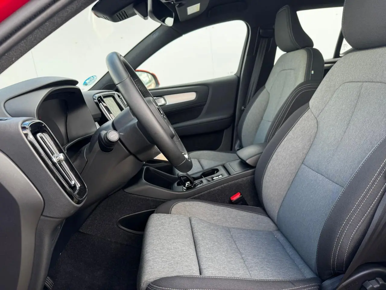 Intérieur avant du Volvo XC40 2024, sièges tissu gris et noir, volant cuir, console centrale avec levier de vitesse.